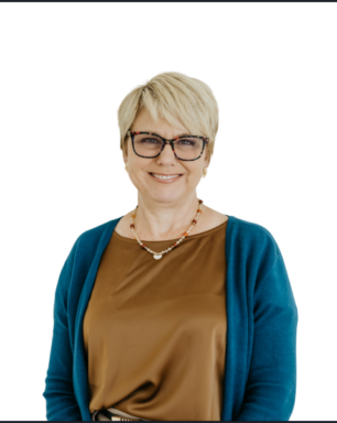 Smiling woman with short blonde hair and glasses, wearing a teal cardigan over a brown satin blouse against a white background.